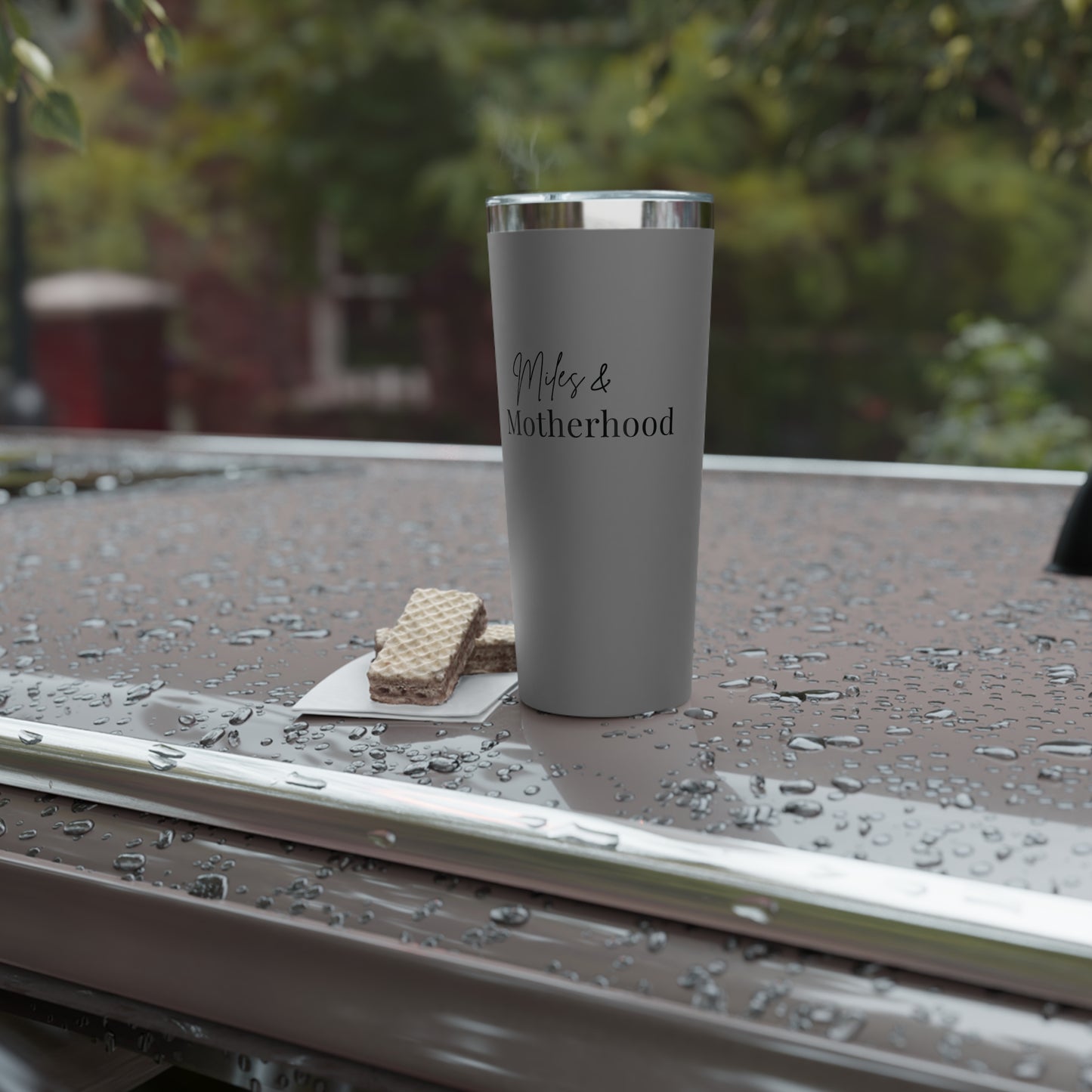 Gray tumbler with 'Miles & Motherhood' text on a wet surface outdoors