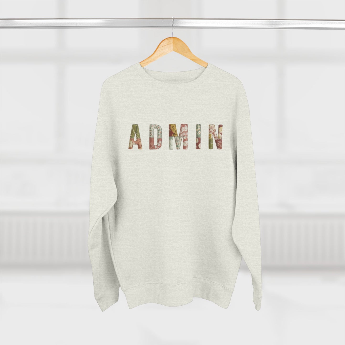 White sweater with 'ADMIN' printed on it hanging on a wooden hanger against a white background