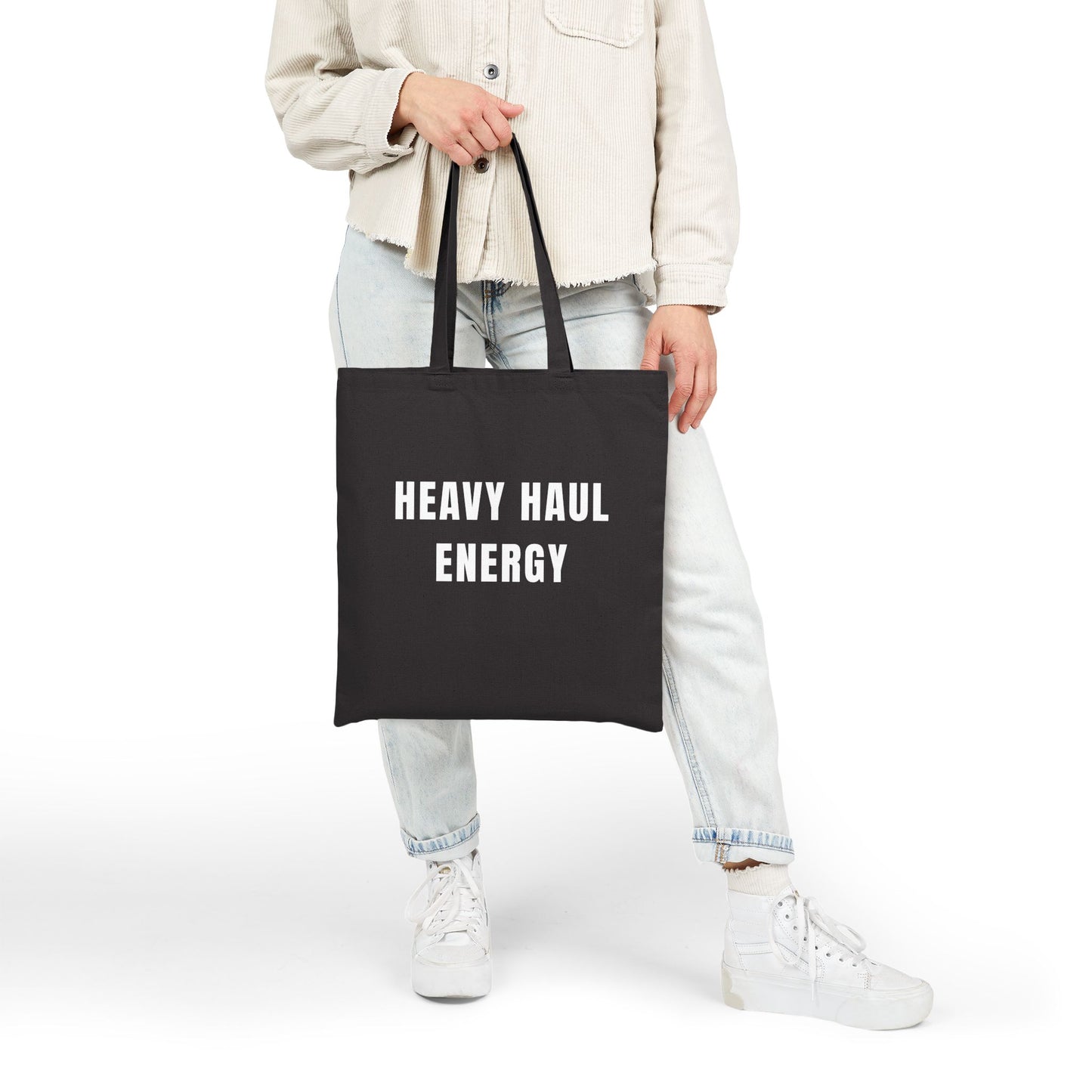 Person holding a black tote bag with 'HEAVY HAUL ENERGY' text on a white background