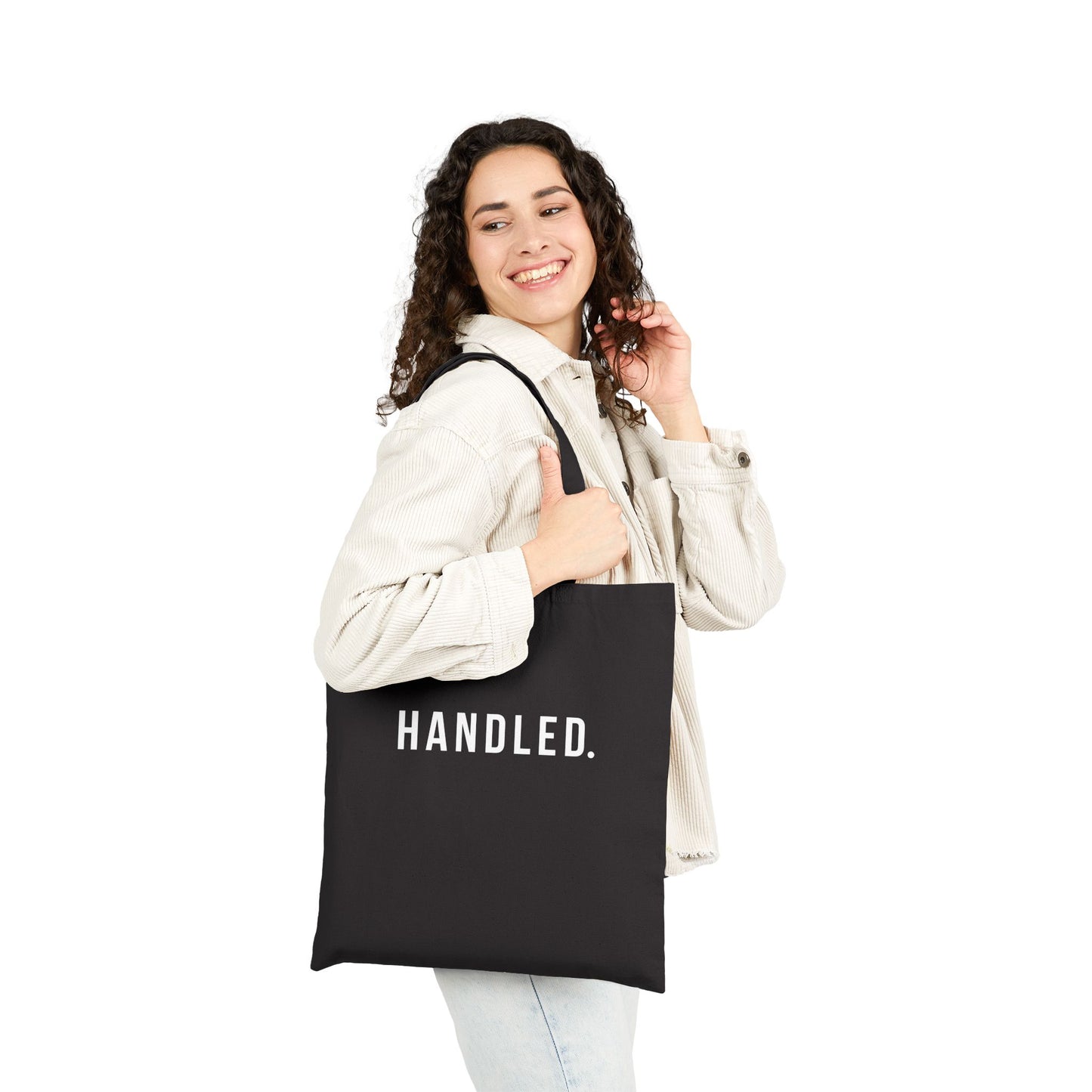 Woman holding a black tote bag with 'Handled' text on a white background