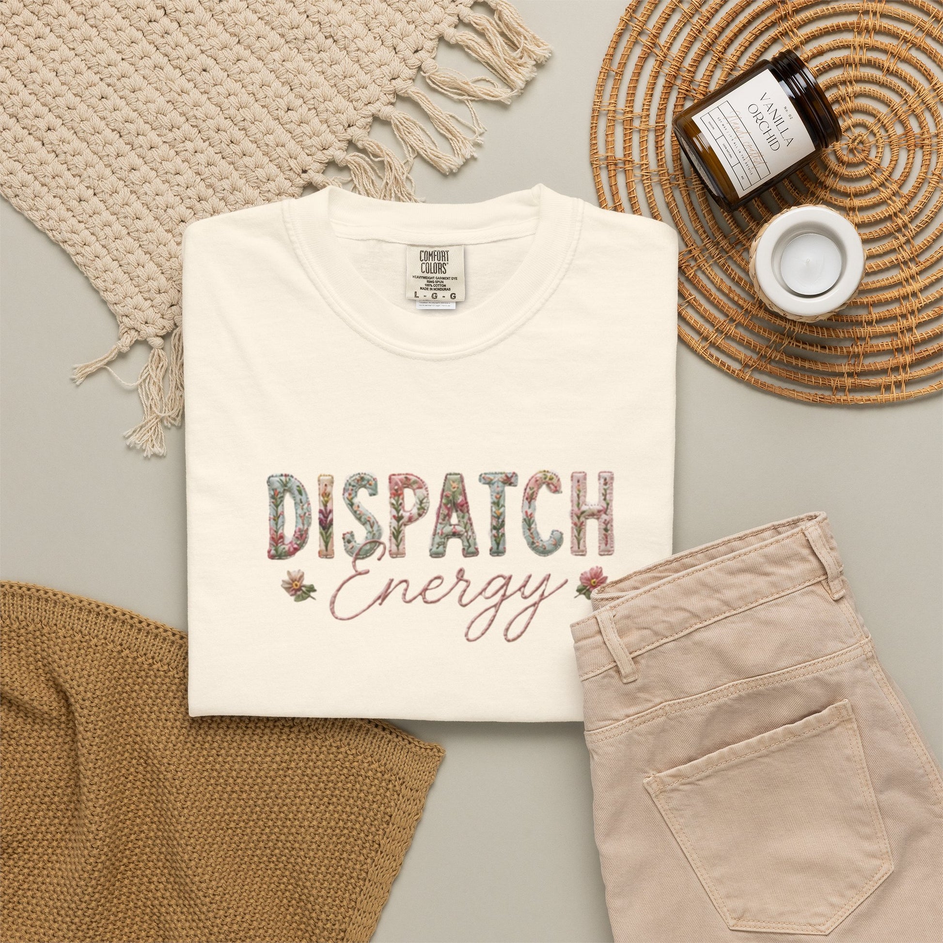 White t-shirt with 'Dispatch Energy' text, beige pants, and decorative items on a light gray surface.