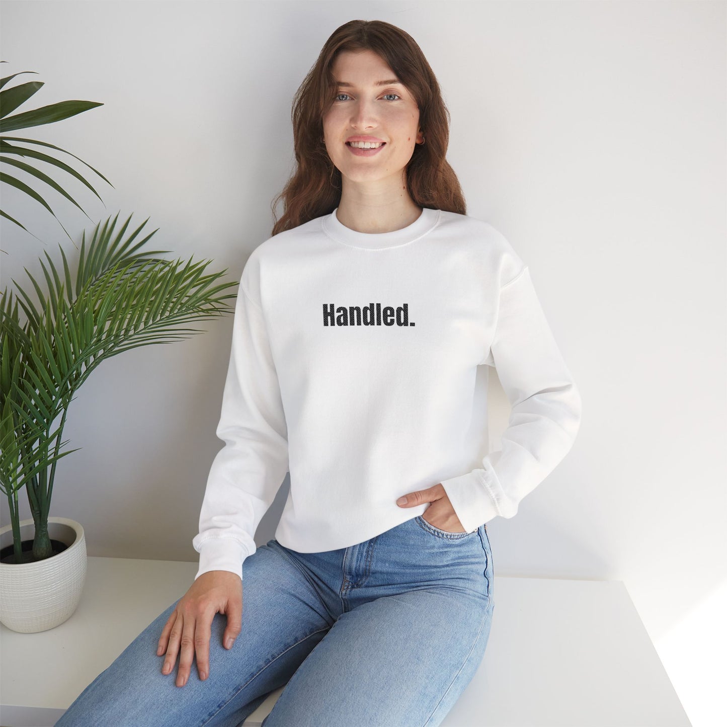 Person wearing a white sweatshirt with 'Handled' text, sitting in a minimalistic room.