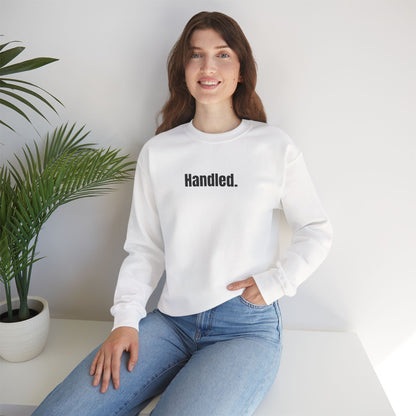 Person wearing a white sweatshirt with 'Handled' text, sitting in a minimalistic room.