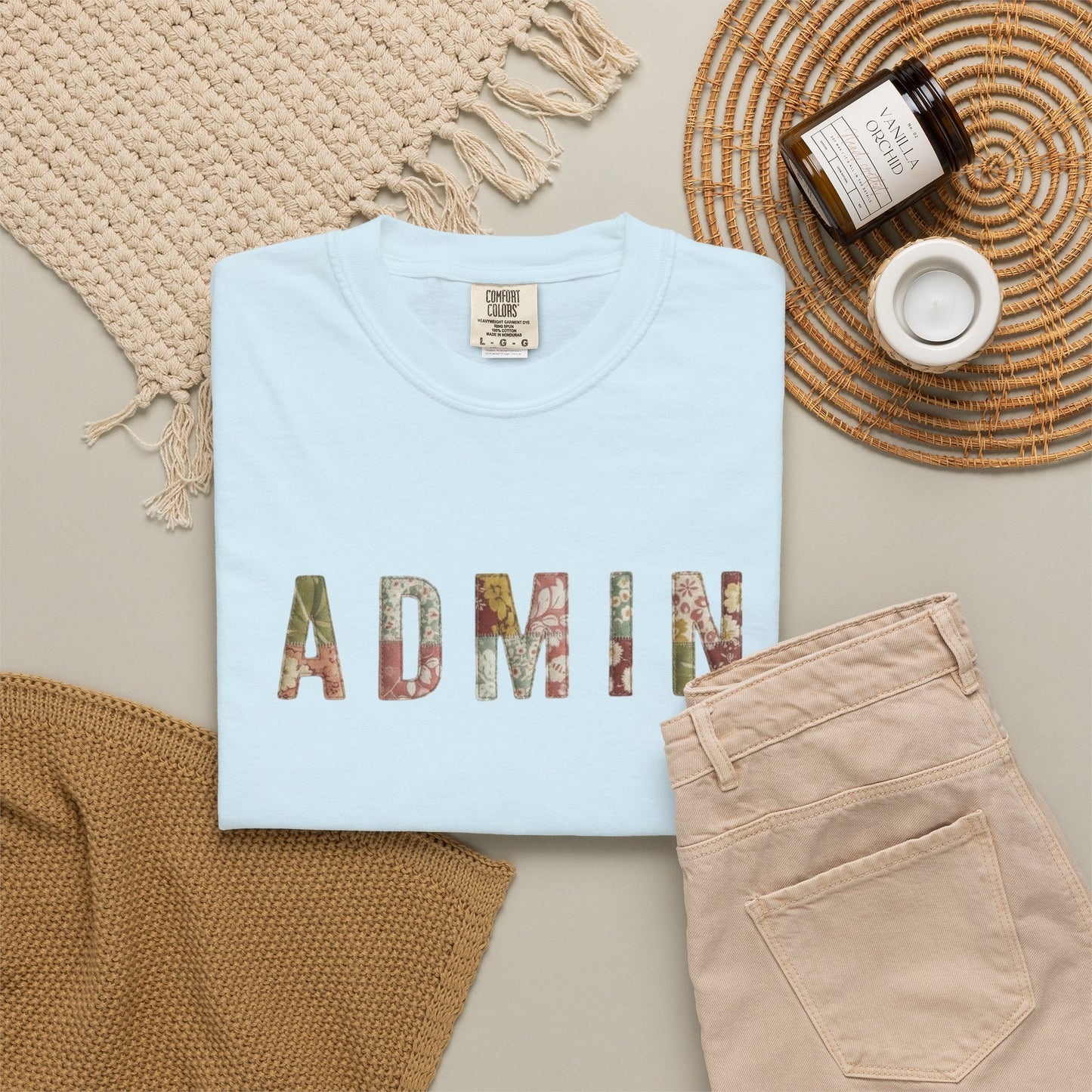 Folded light blue t-shirt with 'ADMIN' print on a neutral surface with accessories.