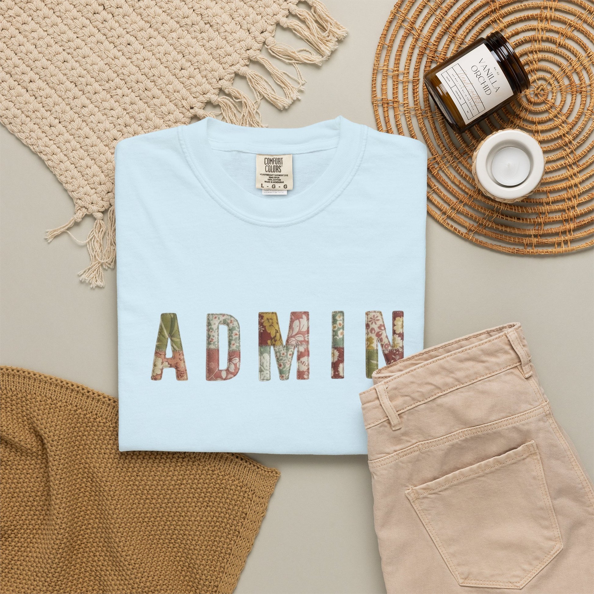 Folded light blue t-shirt with 'ADMIN' print on a neutral surface with accessories.