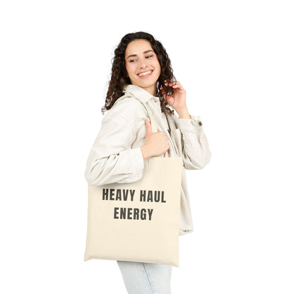 Woman holding a tote bag with 'HEAVY HAUL ENERGY' text on a white background