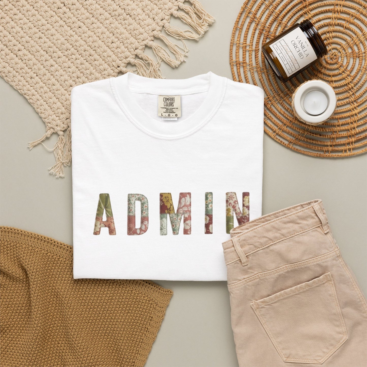 White t-shirt with 'ADMIN' text on a neutral surface with beige pants and decorative items.
