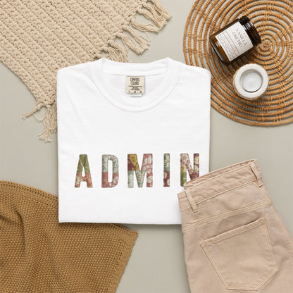 White t-shirt with 'ADMIN' text on a neutral surface with beige pants and decorative items.