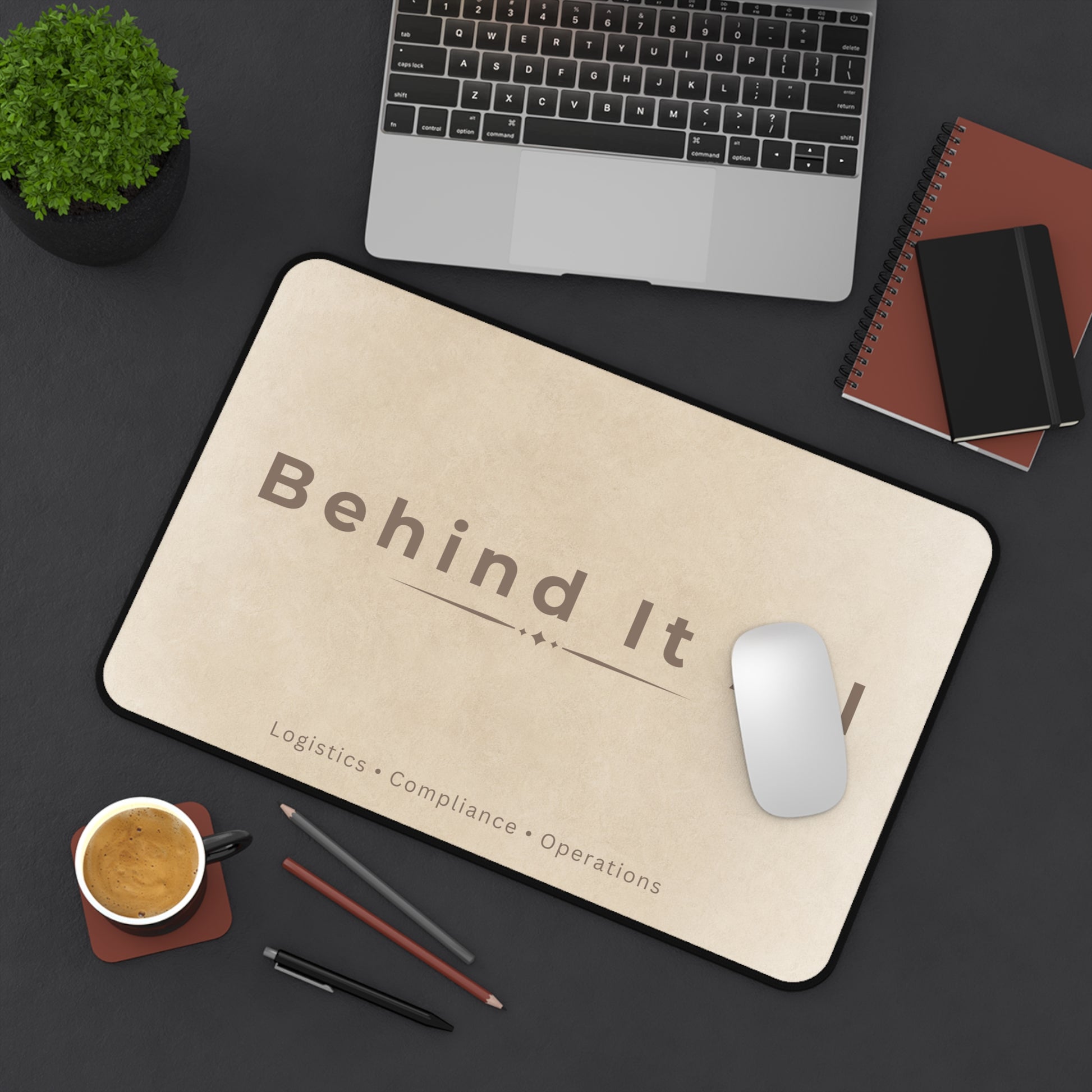 Mouse pad with 'Behind It' branding on a desk with laptop, mouse, and coffee.