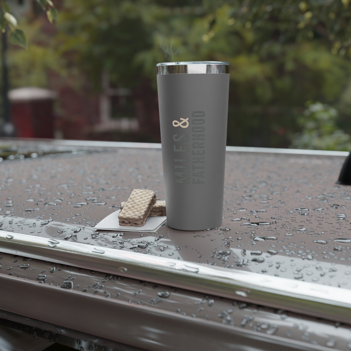 Gray tumbler with a logo on a wet surface outdoors