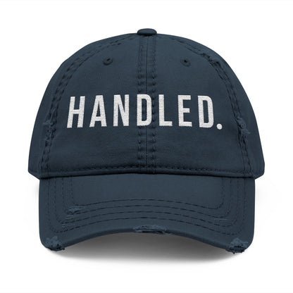 Navy blue cap with 'HANDLED.' text on a white background