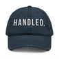 Navy blue cap with 'HANDLED.' text on a white background