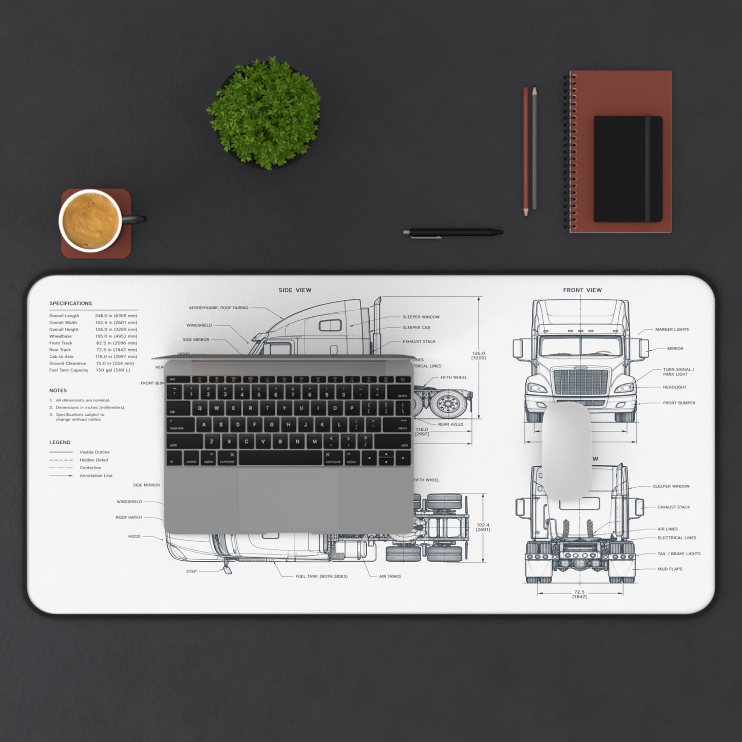 Desk setup with a large desk mat featuring a truck blueprint, laptop, cup, plant, and stationery items on a dark surface.