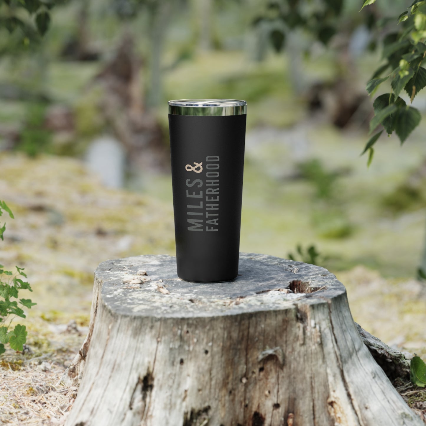 Black tumbler with 'Miles & Fatherhood' text on a wooden stump outdoors