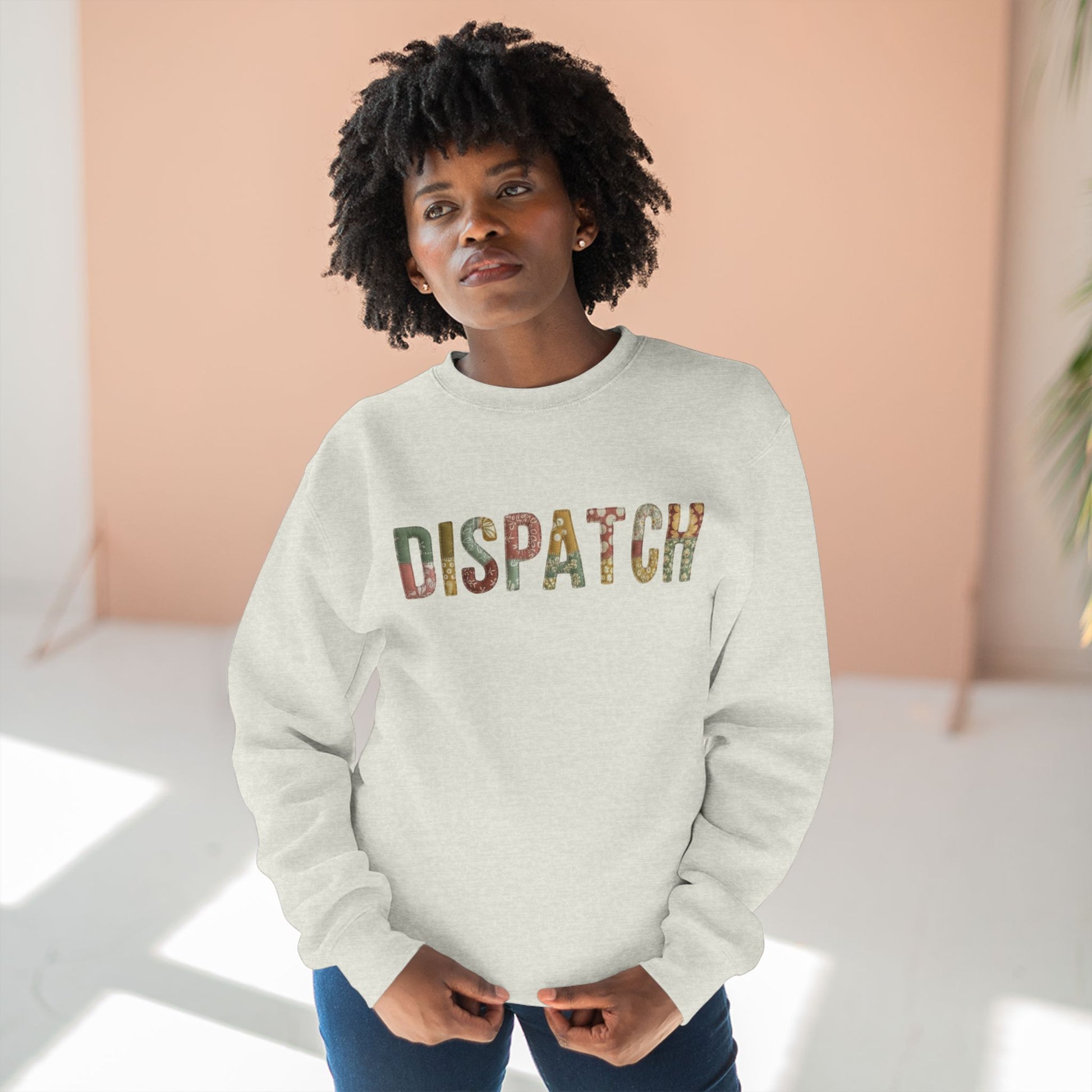 Person wearing a light gray sweatshirt with 'DISPATCH' printed on it against a pink and white background