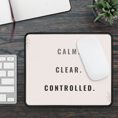 Mouse pad with 'CALM. CLEAR. CONTROLLED.' text on a desk with keyboard and plant