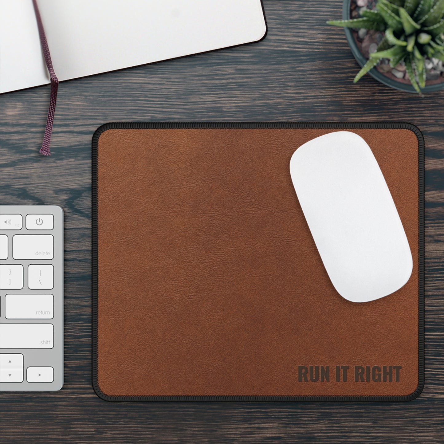 Brown mouse pad with 'RUN IT RIGHT' text on a wooden desk with a keyboard and plant.