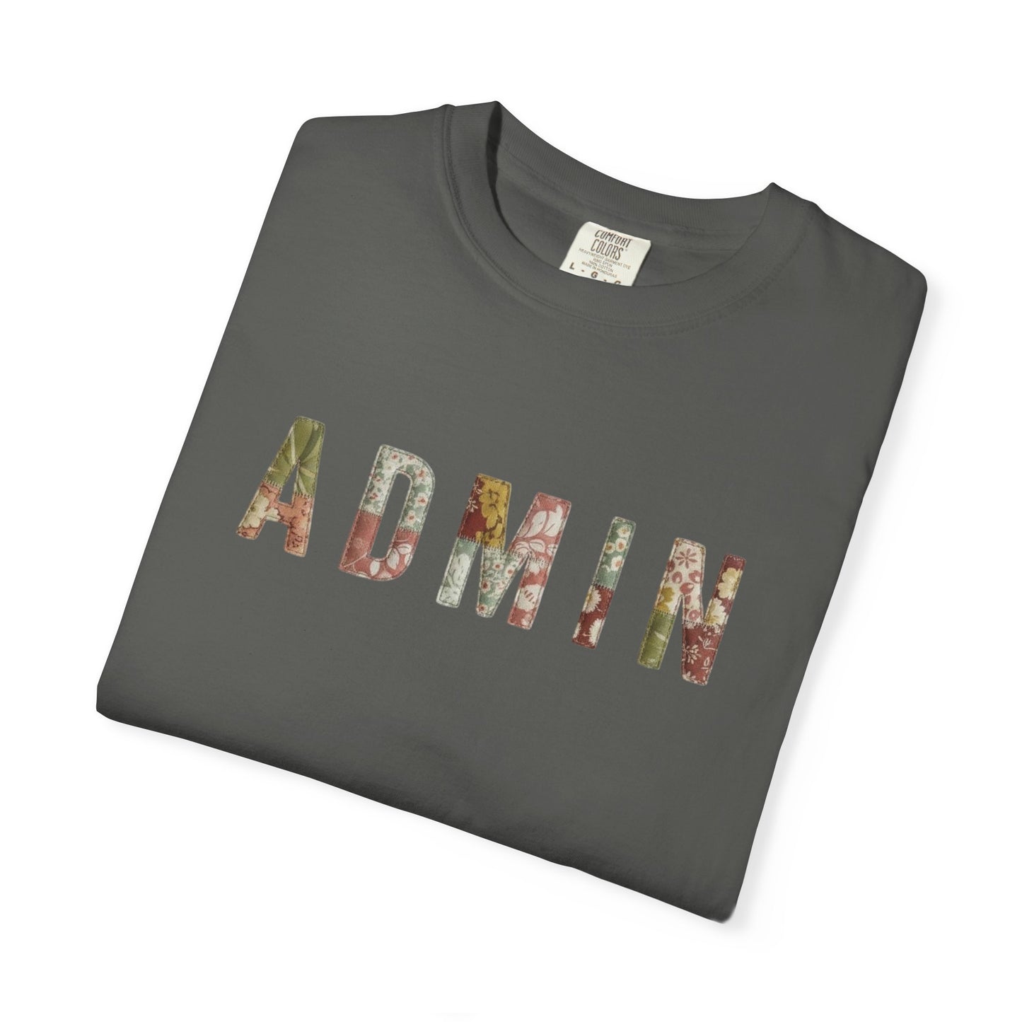 White t-shirt with 'ADMIN' text on a neutral surface with beige pants and decorative items.