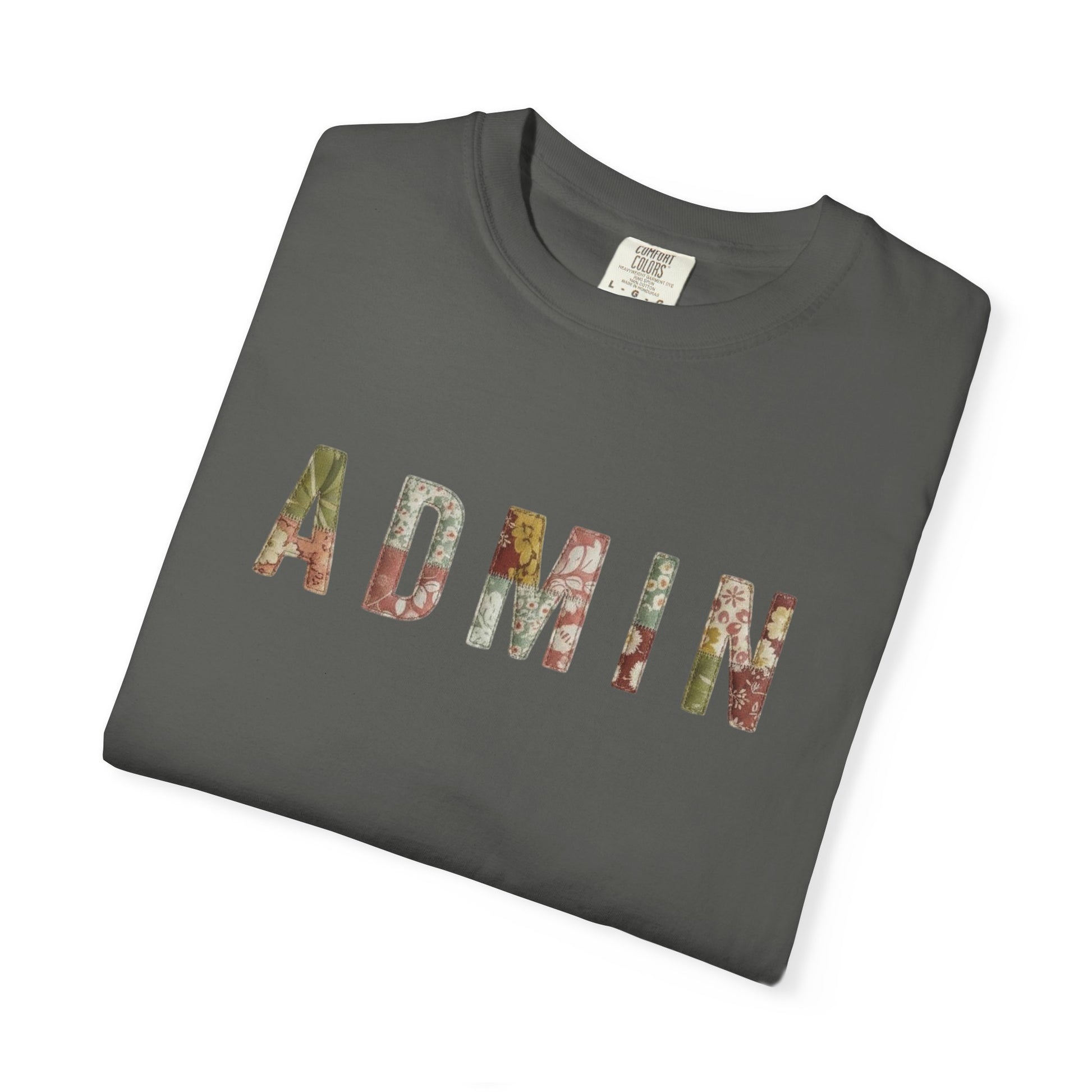 White t-shirt with 'ADMIN' text on a neutral surface with beige pants and decorative items.
