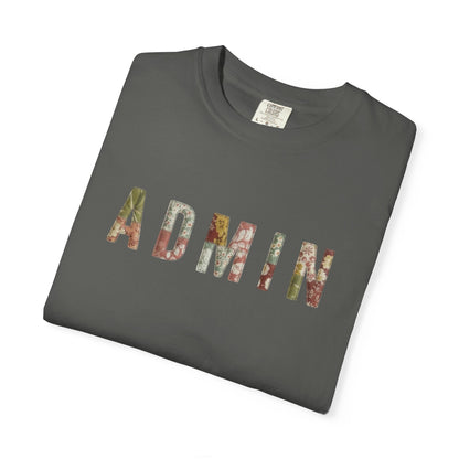 White t-shirt with 'ADMIN' text on a neutral surface with beige pants and decorative items.