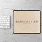 Beige mouse pad with 'Behind It All' text on a marble surface with a keyboard.
