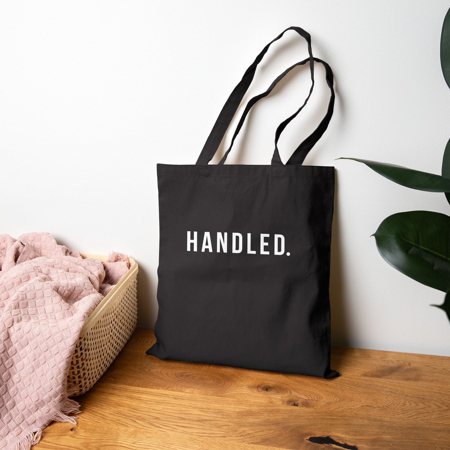 Black tote bag with 'Handled' text on a wooden surface with a plant in the background