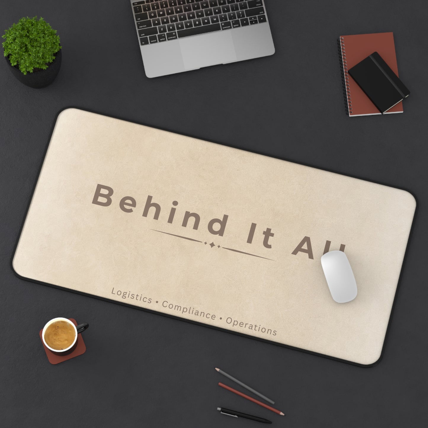 Beige mouse pad with 'Behind It All' text on a dark desk with office items.