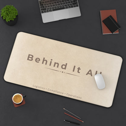 Beige mouse pad with 'Behind It All' text on a dark desk with office items.