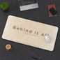 Beige mouse pad with 'Behind It All' text on a dark desk with office items.