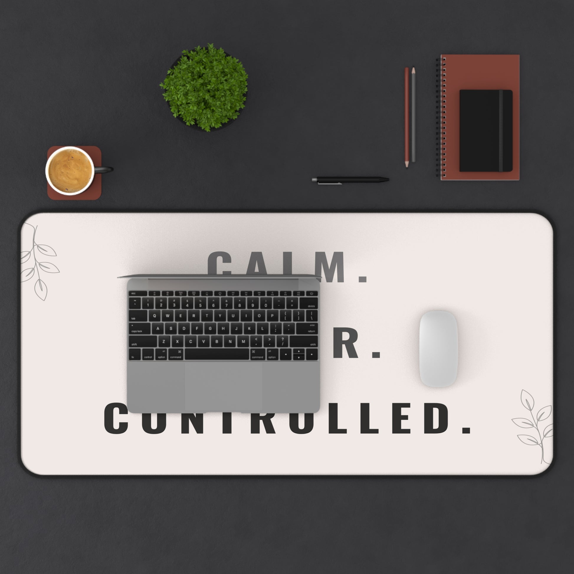 Desk setup with a laptop, mouse, and decor items on a desk mat with text.