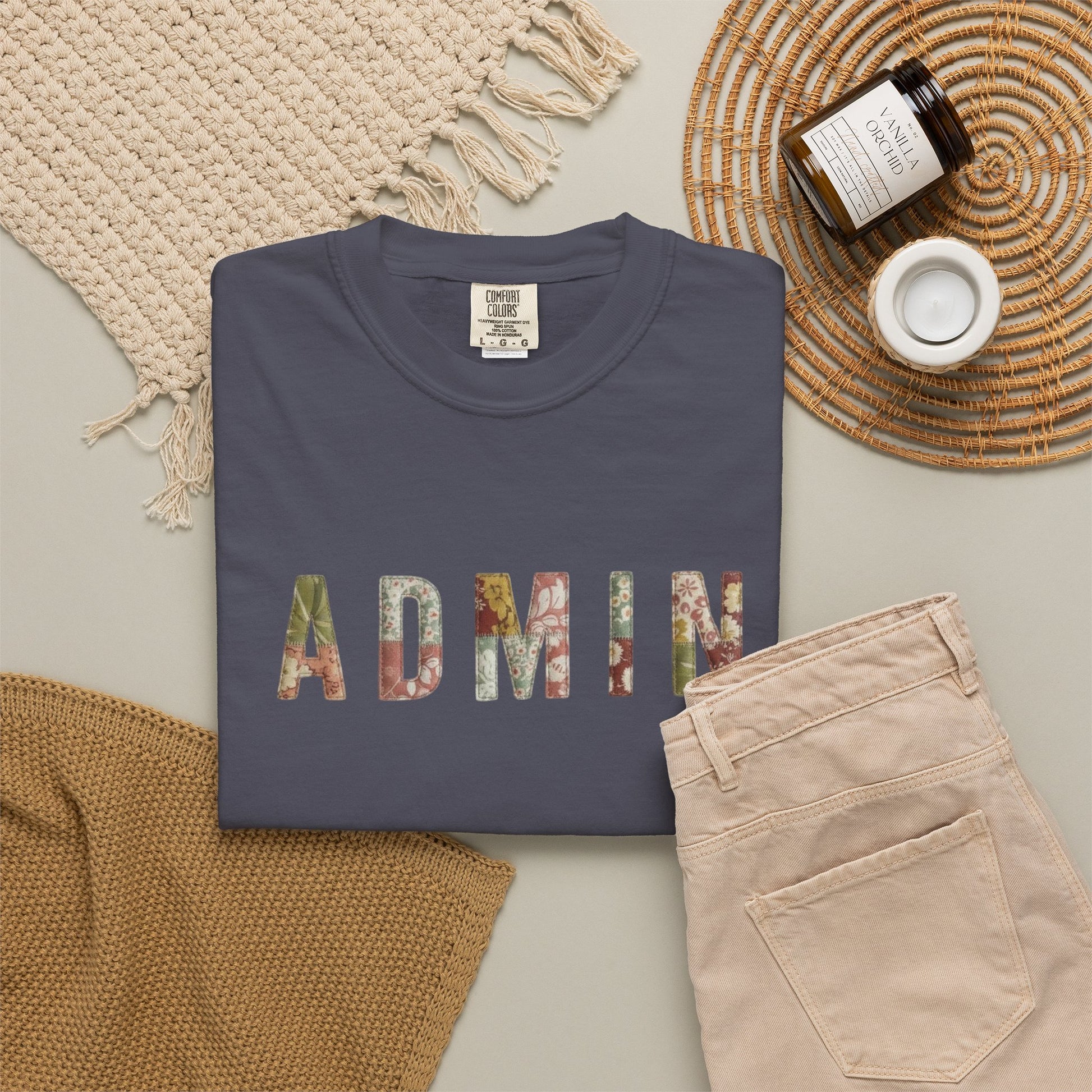 Navy blue sweatshirt with 'ADMIN' in colorful letters on a light surface with beige pants and a woven mat.