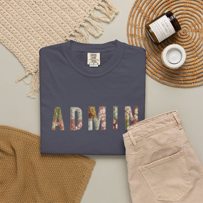 Navy blue sweatshirt with 'ADMIN' in colorful letters on a light surface with beige pants and a woven mat.