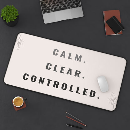 Desk setup with a mouse pad featuring 'Calm. Clear. Controlled.' text, laptop, phone, and coffee cup.
