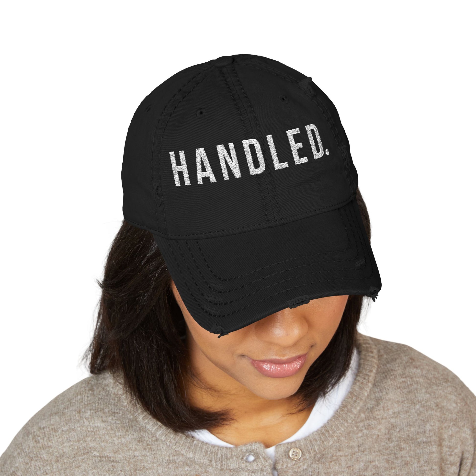 Black cap with 'HANDLED.' text worn by a person on a white background