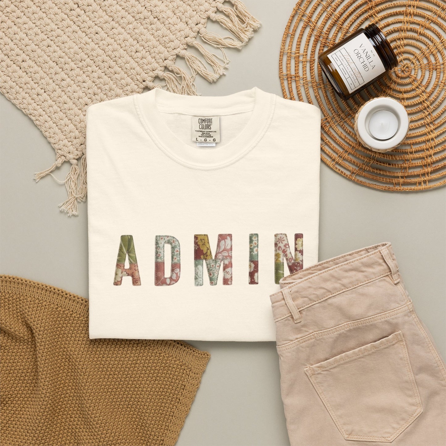 White t-shirt with 'ADMIN' printed on it, beige pants, and a woven mat on a light gray surface.