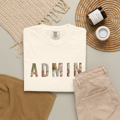 White t-shirt with 'ADMIN' printed on it, beige pants, and a woven mat on a light gray surface.
